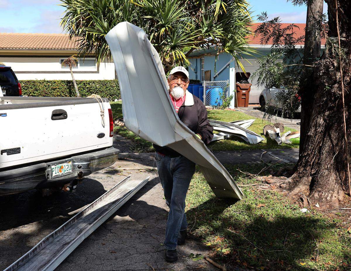 A neighbor salvages pieces of awning as residents and the City of Hialeah clean up downed fences, trees, and awnings after a tornado touched down near the Garden of the Arts park in Hialeah, Florida on Monday, Jan. 28, 2019.