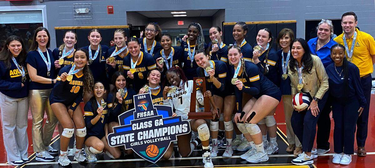 St. Thomas Aquinas players and coaches gather with the state championship trophy after winning the Class 6A girls volleyball state title game against Gulf Breeze on Saturday at Polk State College in Winter Haven, Fla.