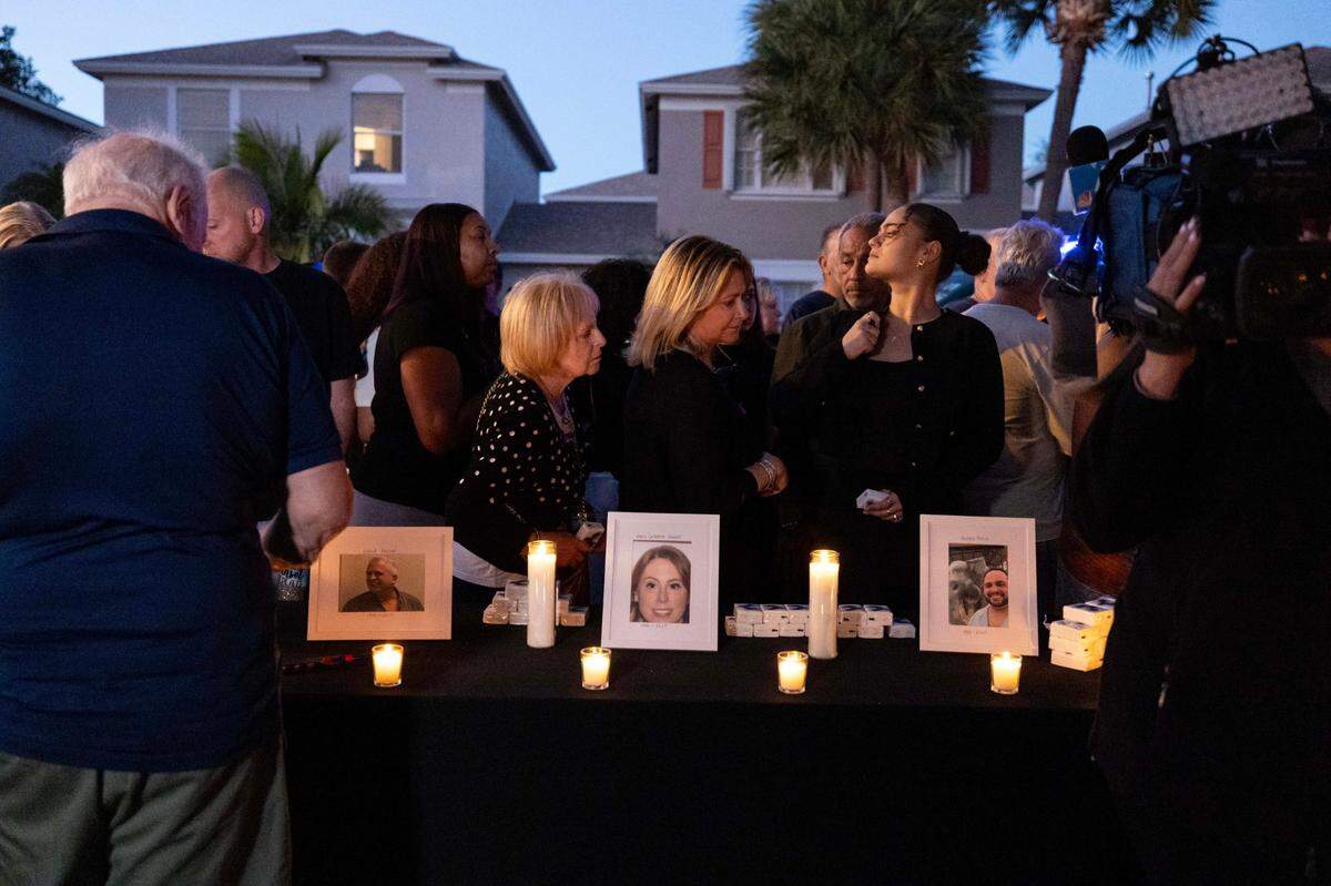 People walk past portraits of the victims of a triple murder inside the Plum Bay community during a candlelight vigil on Sunday, Feb. 23, 2025, in Tamarac, Florida.