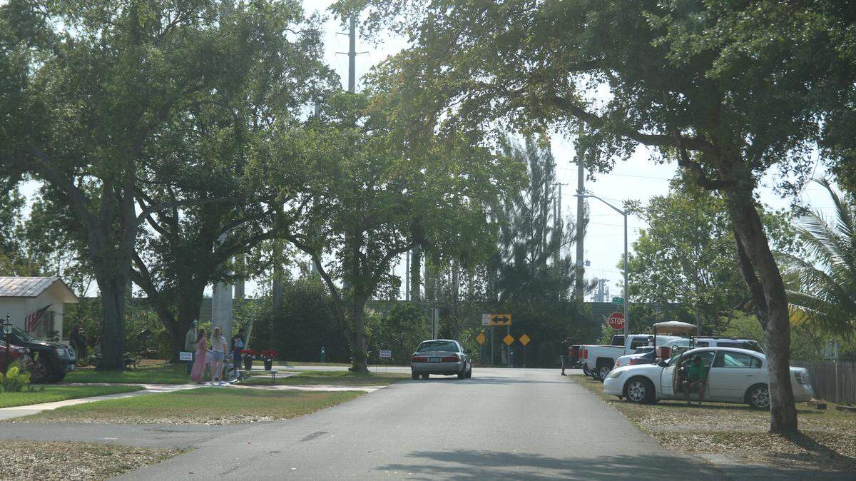 Mask-wearing mourners park and wait their turn to collect roses at a drive-by memorial on Good Friday for former Miami Springs Councilman Jim Caudle.