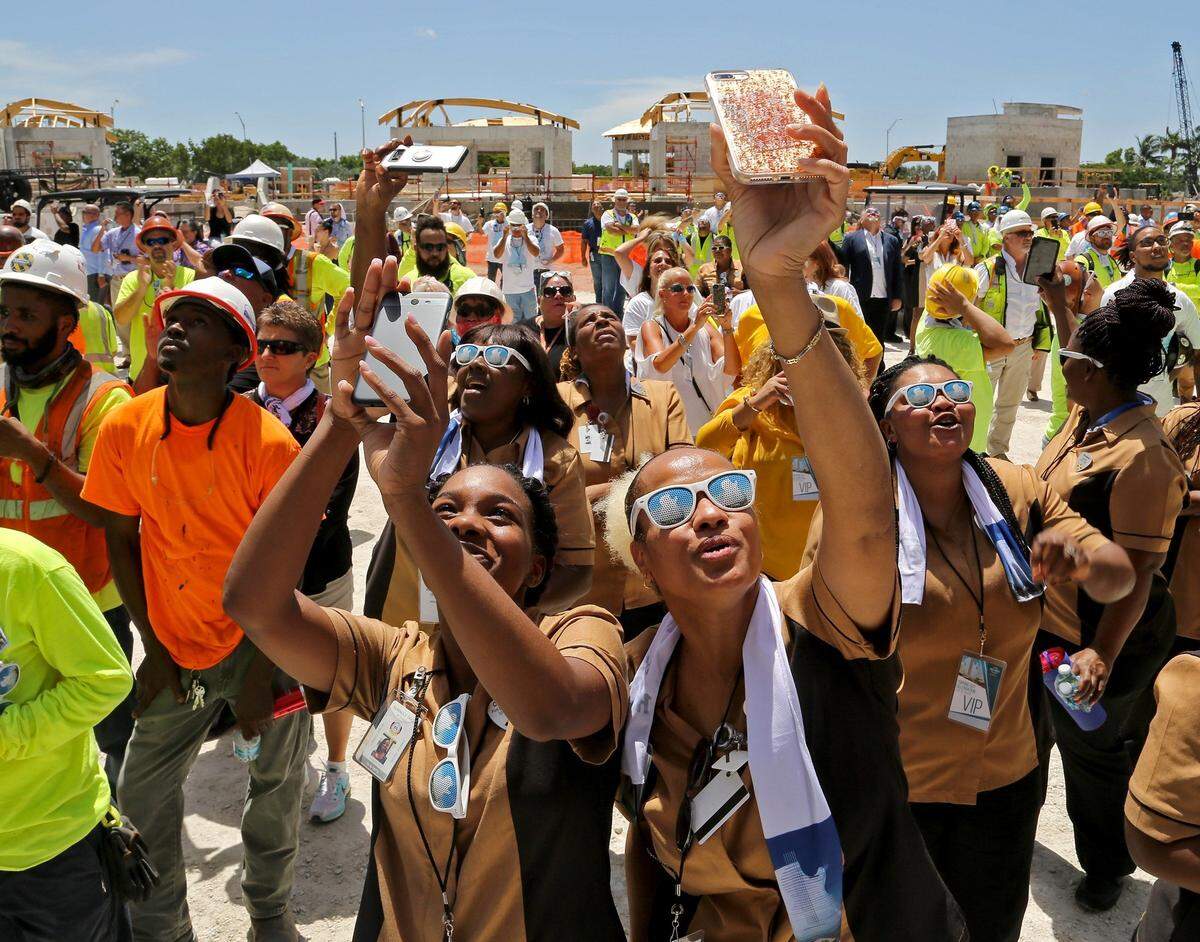 Housekeepers Chaquana Jones, 27, left-center, and Audrey Boykin, right-center, 49, lift up their cellphone as they and hundreds of employees and construction workers watch the "topping out" ceremony for Seminole Hard Rock Hotel & Casino Hollywood's guitar-shaped hotel on Monday, July 9, in Hollywood.