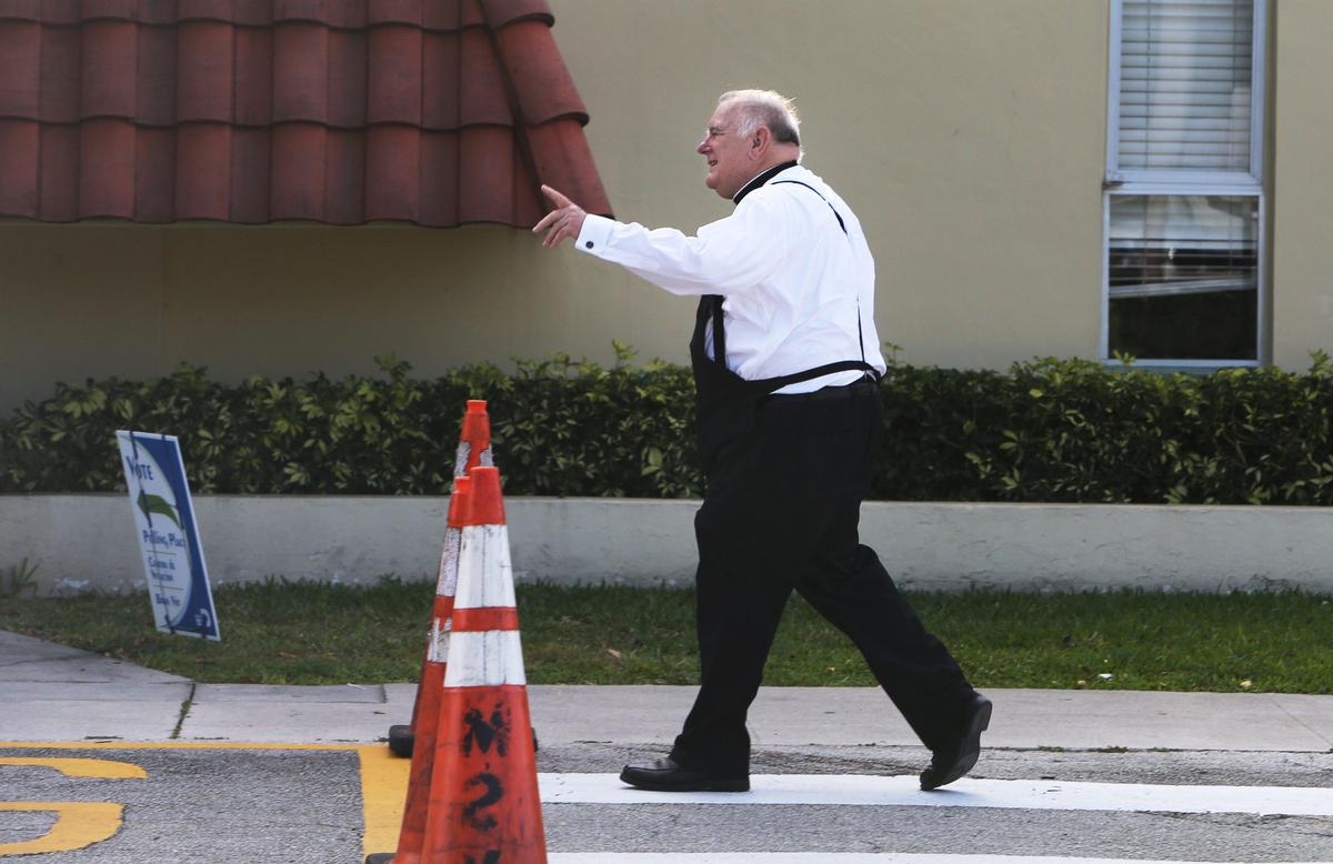 Miami Archbishop Thomas Wenski waves to fellow voters as he walks into The C. Lawton McCall Community Center in Miami Shores to vote in the Florida Primary, Tuesday, March 17, 2020.