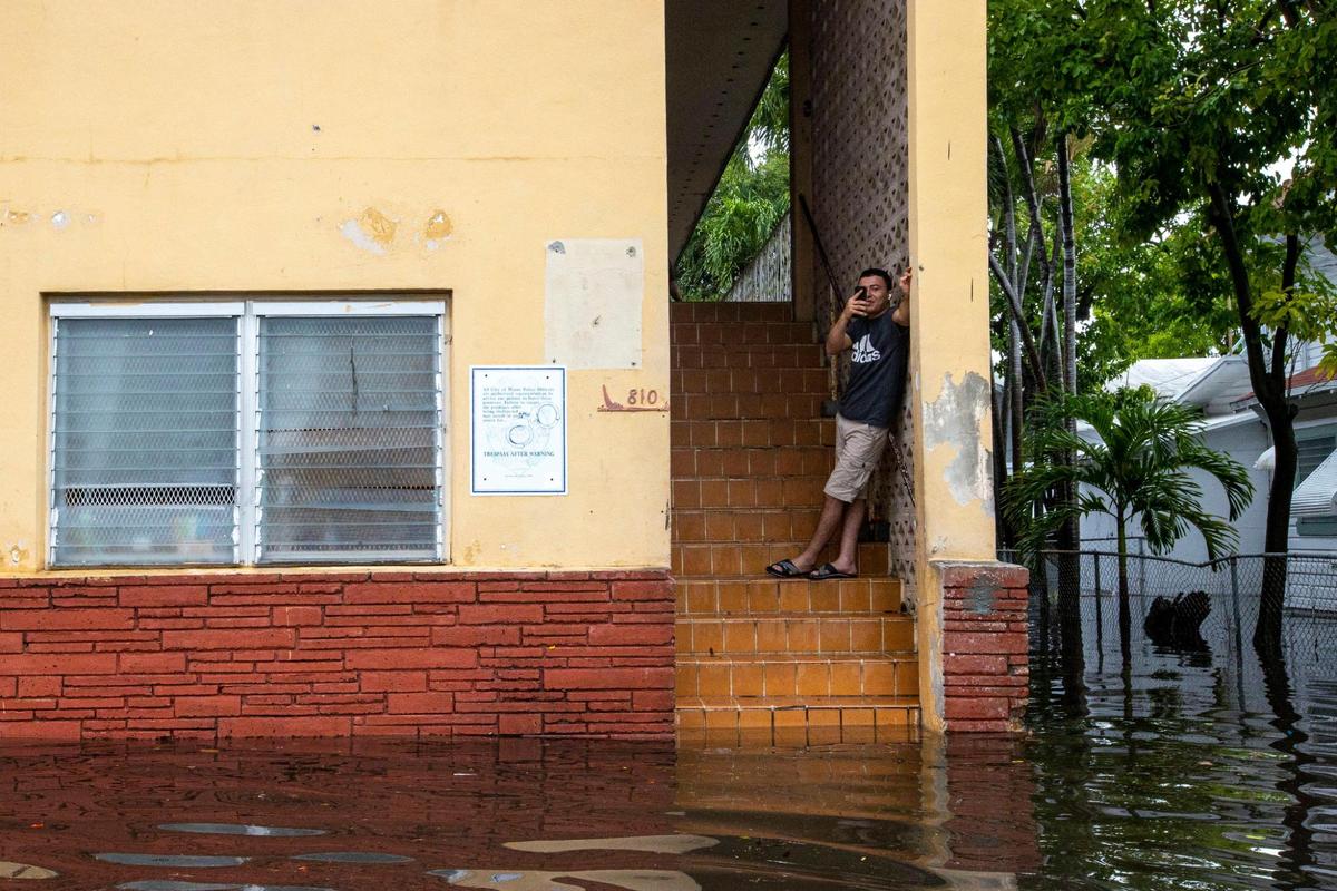 A man records the floodwaters as he stays dry atop the stairs off Southwest Third Street and Eighth Avenue in the Little Havana neighborhood of Miami, Florida, on Saturday, June 4, 2022. Older buildings like these in low-lying areas could be at risk for more flooding in the future as sea levels rise, which could lead to property buyouts.