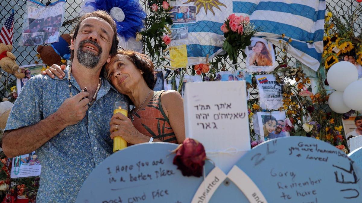 Bernardo and Maria Ines Camou, whose sister Maria Gabriela Camou died in the June 24 Surfside condo collapse, visit a makeshift memorial to the 98 victims of the Champlain Towers South tragedy on July 14, 2021.