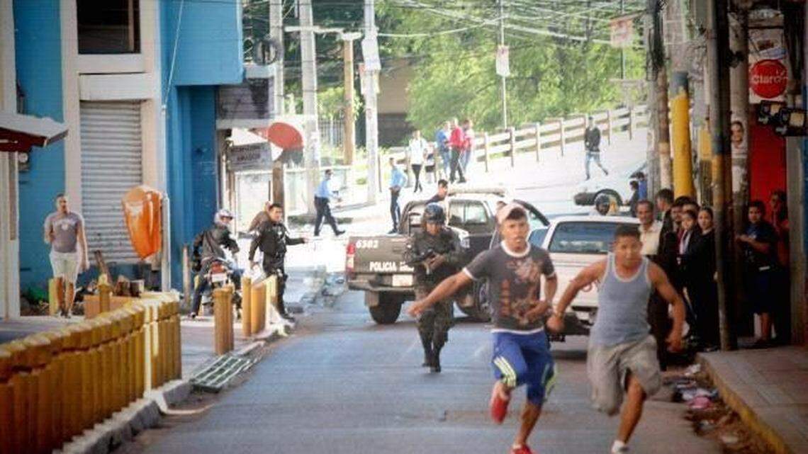 In a photo taken by Honduran human rights observer César Fuentes on Dec. 1, 2017, a member of the Honduran military police is seen firing a M4 rifle at two young men fleeing, after officers broke up an anti-government protest in the center of Tegucigalpa. Fuentes said bullets were flying everywhere, and he checked himself for bullet wounds after taking the photo.