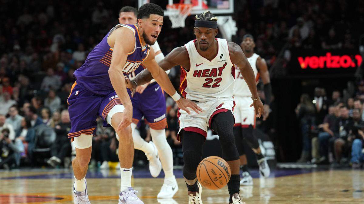 Phoenix Suns guard Devin Booker (1) and Miami Heat forward Jimmy Butler (22) chase a loose ball during the second half at Footprint Center.