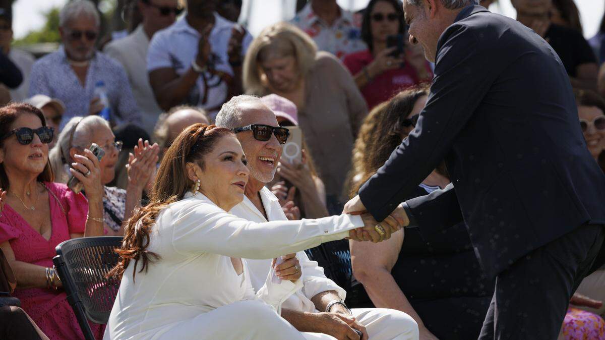 Gloria Estefan shakes hands with Miami Beach Mayor Steven Meiner?? while sitting next to her husband, Emilio Estefan, during a street naming ceremony in honor of Gloria Estefan on Monday, Oct. 13, 2025, at 13th Street and Ocean Drive in Miami Beach, Fla. 