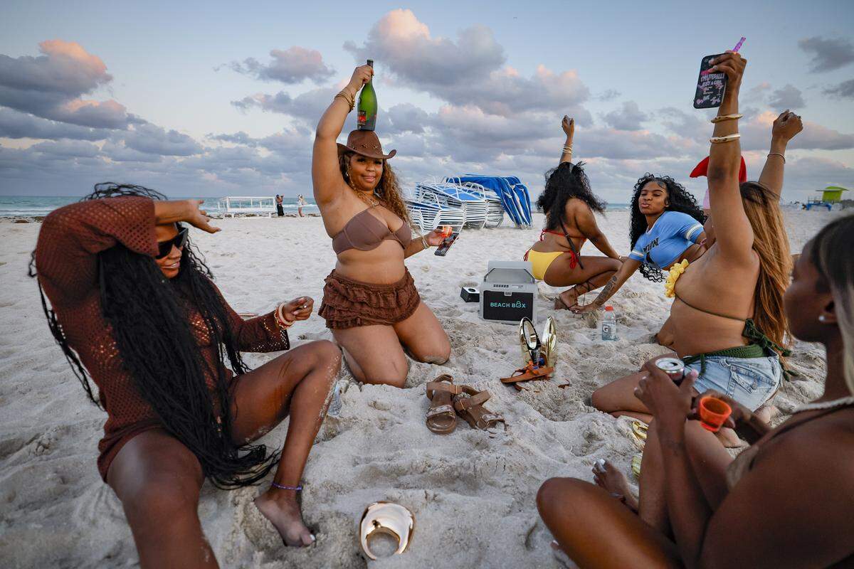 Niy Banks of Delaware, holds a bottle of champagne over her head as she parties with friends and listen to dance music on South Beach during spring break in Miami Beach, Florida on Friday, March 20, 2026.