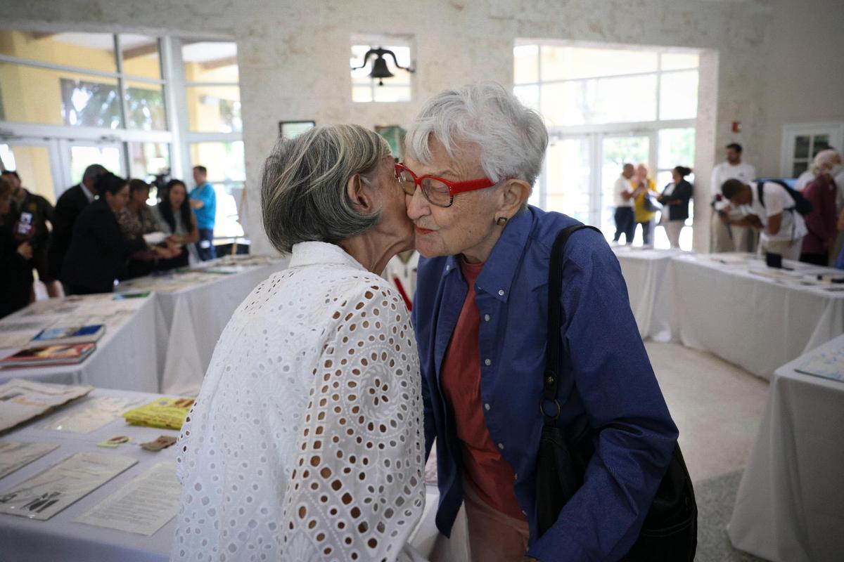 Silvia Unzueta, a Women’s Park founder, left, kisses Freda Tschumy, the artist who designed the time capsule, during the unveiling of its contents, pictured behind them, from 31 years ago on Wednesday, March 22, 2023, at The Women’s Park in Miami.