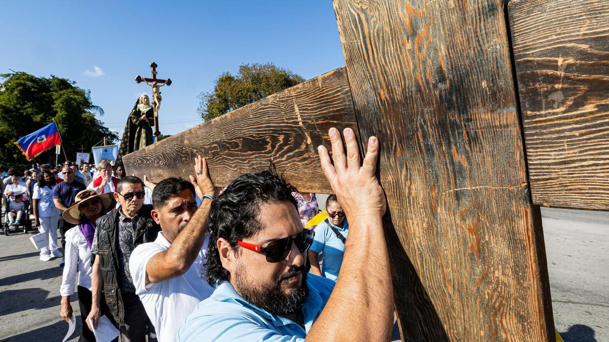 From right to left: Carlos Ruiz, 36, Alberto Bastidas, 47, Roberto Aguirre, 65, and Maria Fernandez, 73, carry a wooden cross during the Living Stations of the Cross procession near the Cathedral of St. Mary on Friday, April 18, 2025, in Miami, Fla.