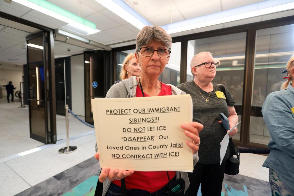 Mariana Lopez, a resident of Miami-Dade County, holds a sign outside the commission chambers after the cancellation of a County Commission committee hearing on Monday, June 9, 2025. The matter of the hearing was regarding reimbursement for extended detention in county jails of inmates booked on local charges but also sought for deportation.