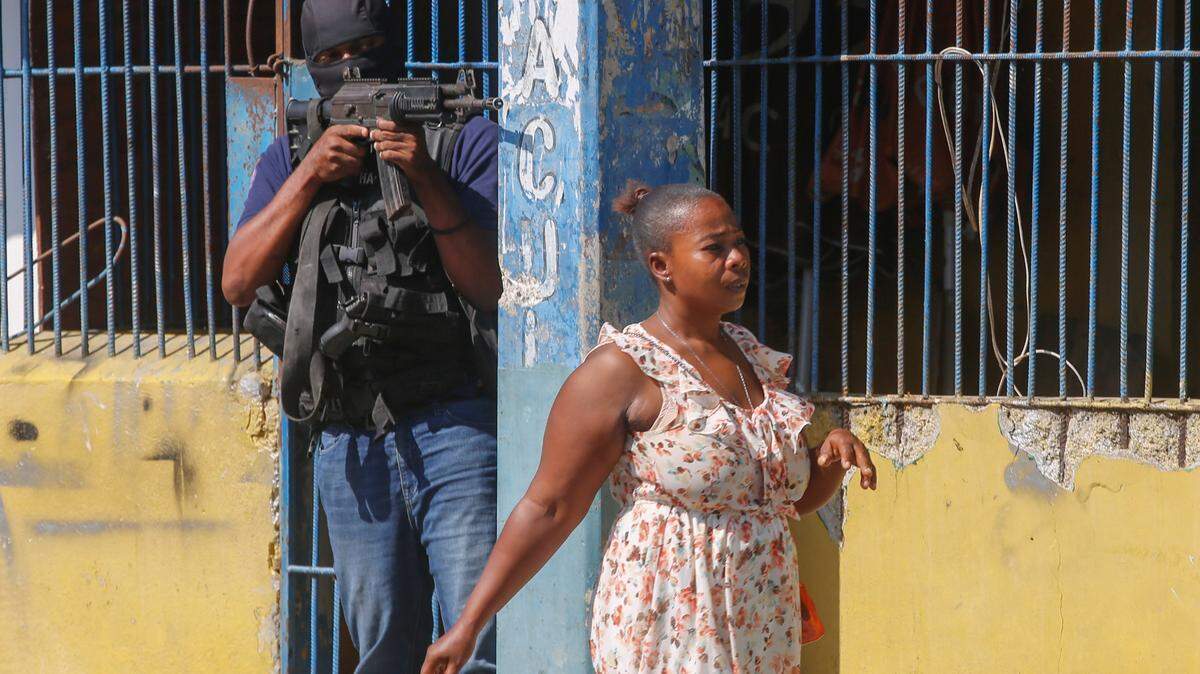 A resident walks past a National Police officer guarding the empty National Penitentiary after a fire inside the jail in downtown Port-au-Prince, Haiti, Haiti, Thursday, March 14, 2024. This is the same prison that armed gangs stormed late March 2 and hundreds of inmates escaped. (AP Photo/Odelyn Joseph)