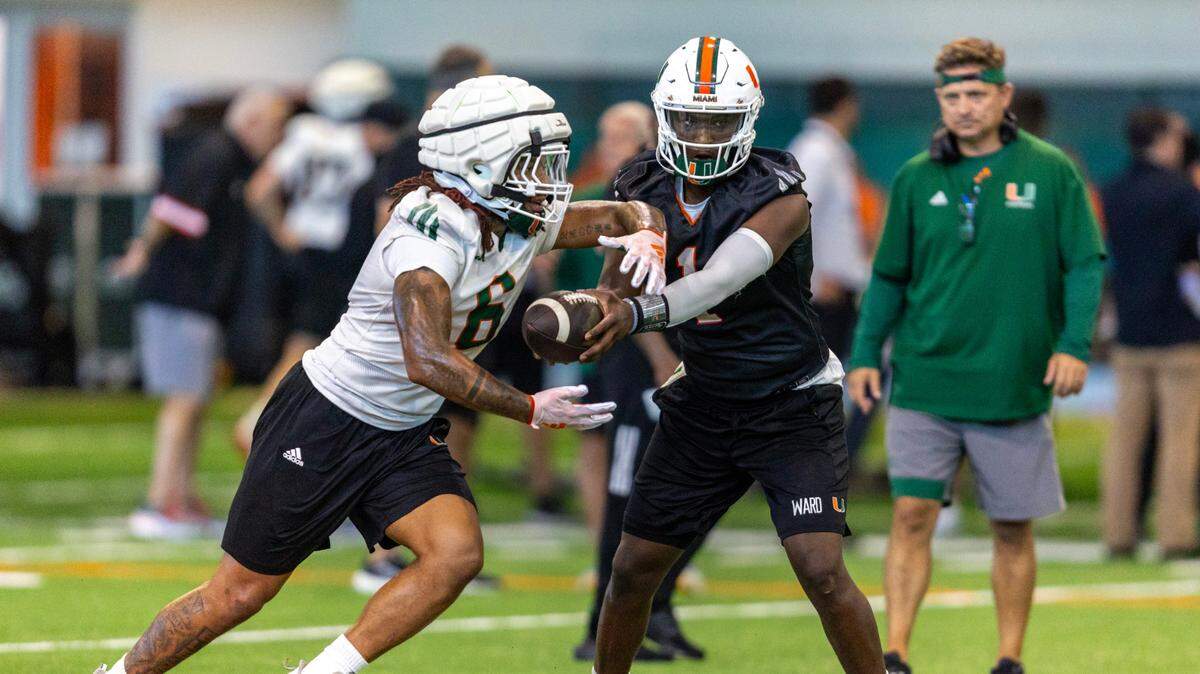 Miami Hurricanes quarterback Cam Ward (1) hands off the ball to running back Damien Martinez (6) during practice at the Carol Soffer Indoor Practice Facility on Thursday, August 1, 2024, in Coral Gables, Fla.