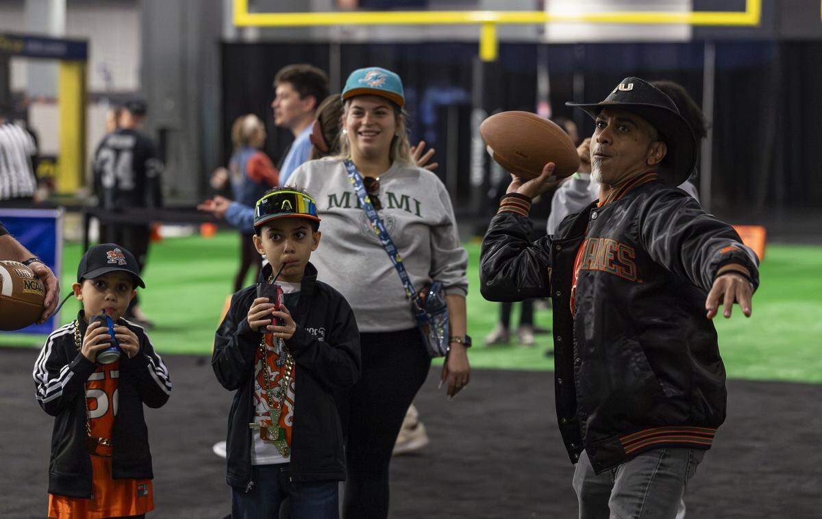 Victor Villafañe throws a football while his kids, Aiden, 9, center, and Ethan, 6, watch during the Playoff Fan Central at the Miami Beach Convention Center on Friday, Jan. 16, 2025, in Miami Beach, Fla. Fans can visit the event ahead of the College Football Playoff National Championship Game between the Miami Hurricanes and the Indiana Hoosiers and enjoy a variety of family-friendly interactive experiences.