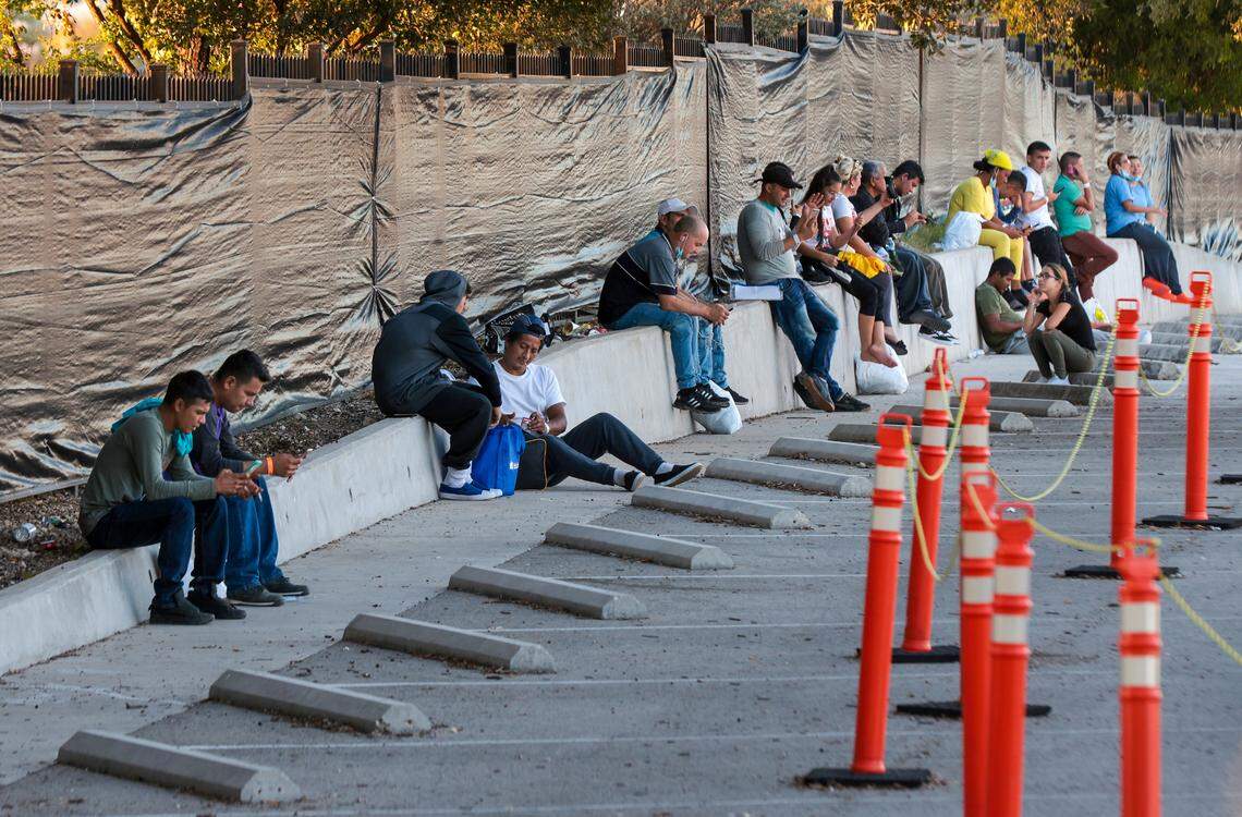 Venezuelan migrants sit and attend to their cellphones in the closed parking lot of San Antonio’s Migrant Resource Center.