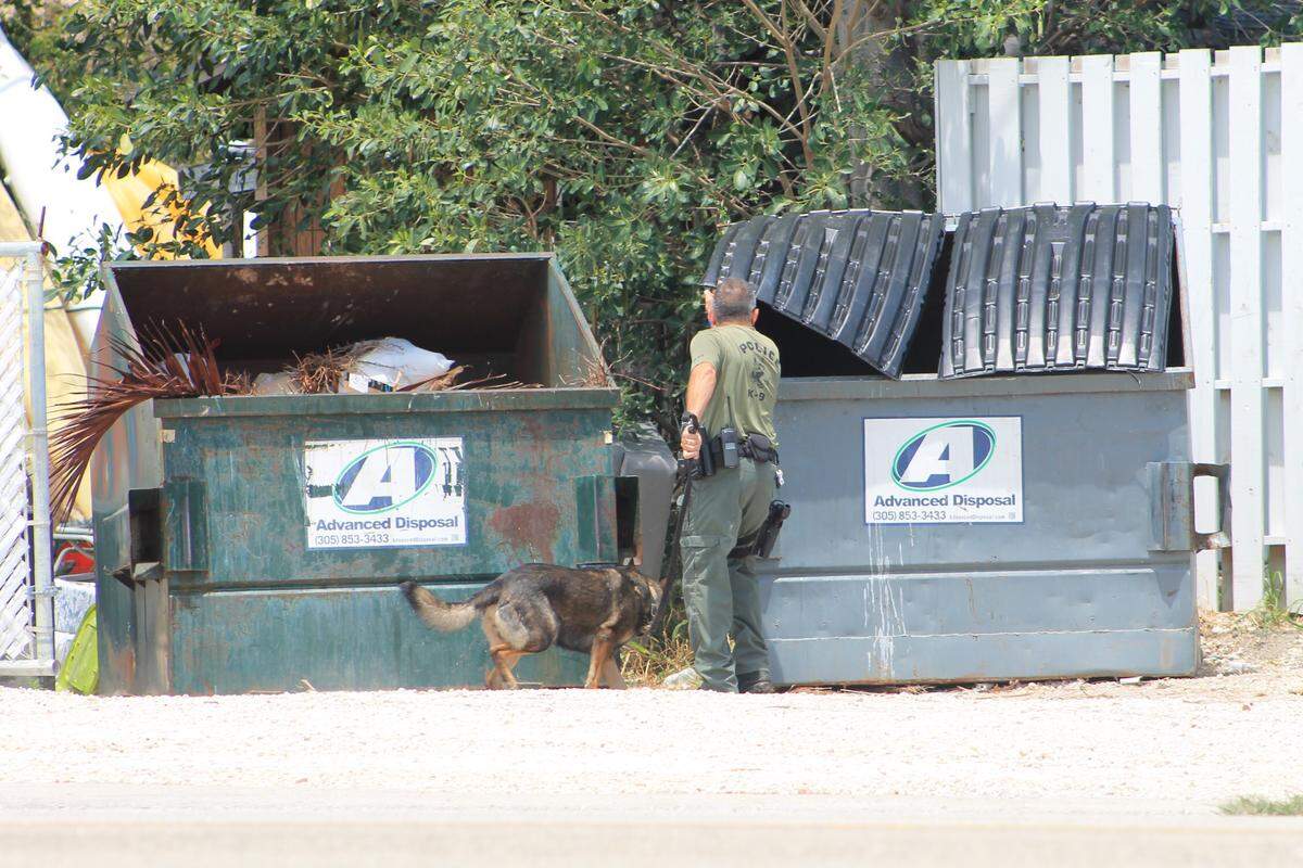 A police officer and his K9 search a dumpster outside of the Executive Bay Club townhomes in Islamorada, where a 17-year-old boy stabbed his younger brother to death and severely wounded his father Thursday, May 7, 2020.