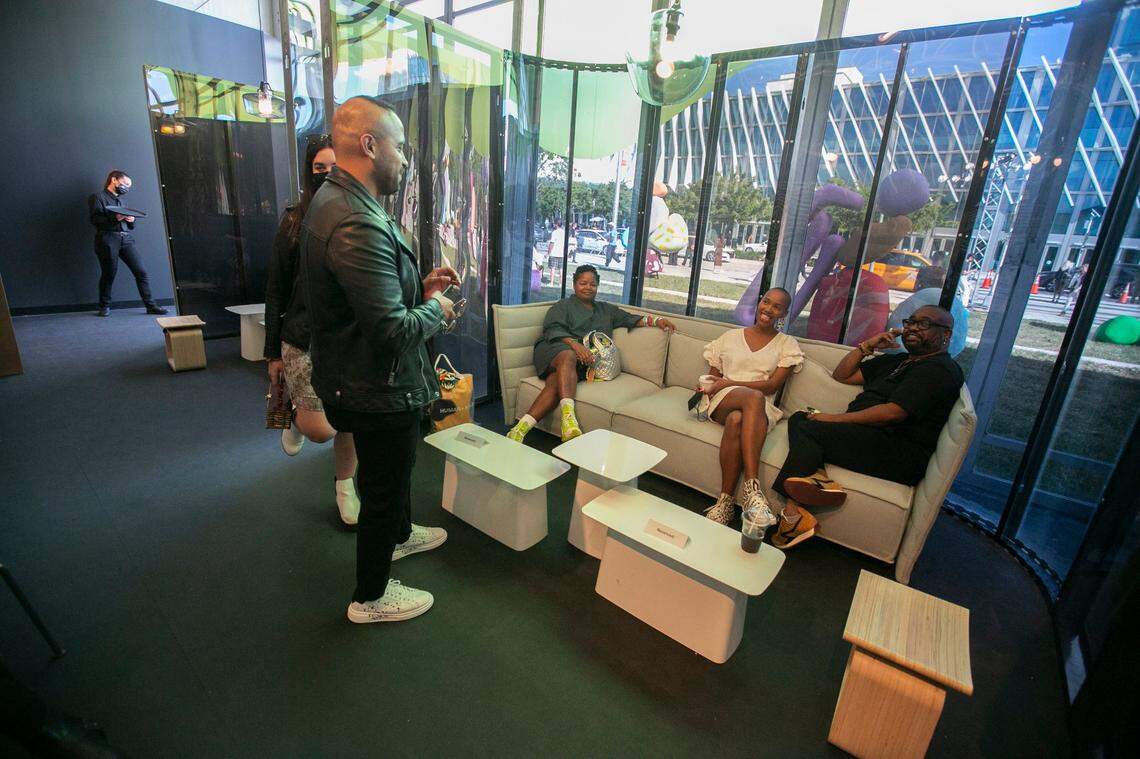 Inside the Perrier-Jouet VIP Lounge, part of the Blackouflage exhibit area at Design Miami, booth designers Danielle Fennoy, center, and Leyden Lewis, right, sit with artist, Glenyse Thompson, left, inside  one of the one-way mirrored booths. The booths are a social commentary on the one-way mirrored interrogation rooms in police stations.
