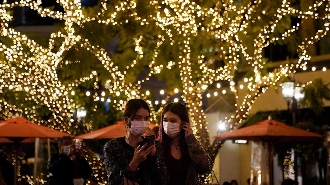 Two people wear masks under a tree decorated for Christmas amid the COVID-19 pandemic in the business district of Los Angeles, California on Dec. 22, 2021. We have another COVID Christmas on our hands - here’s how you can celebrate safely this year.