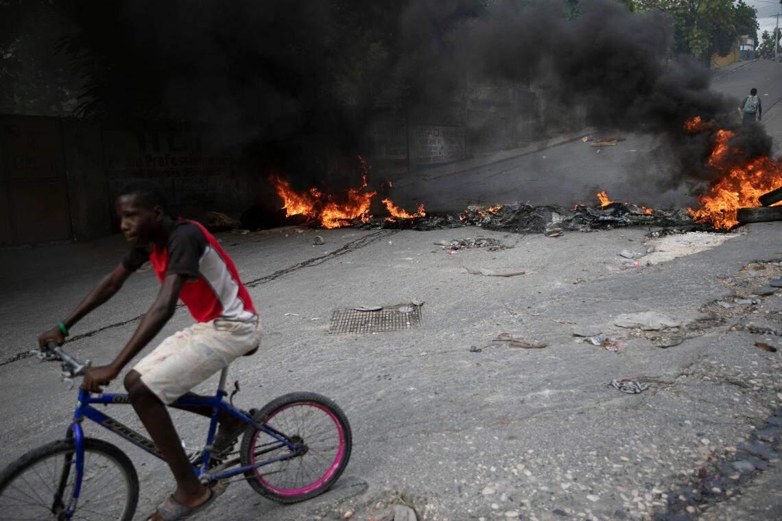 A man rides his bicycle past a burning barricade during a protest over the death of journalist Romelson Vilcin , in Port-au-Prince, Haiti, Sunday, Oct. 30, 2022.
