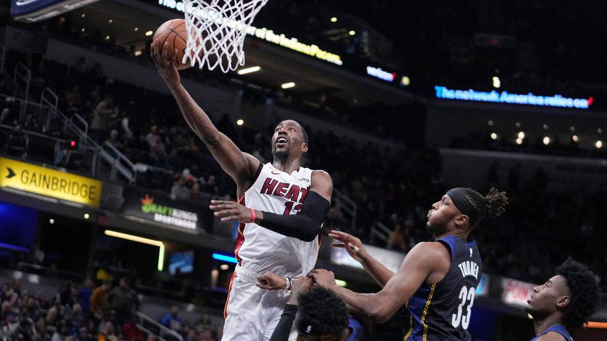 Miami Heat’s Bam Adebayo puts up a shot against Indiana Pacers’ Oshae Brissett and Myles Turner (33) during the first half of an NBA basketball game, Monday, Dec. 12, 2022, in Indianapolis.