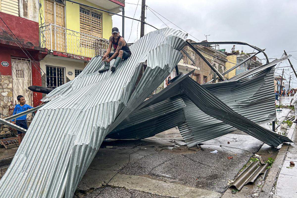 A resident sits on part of the roof of his house, damaged by Hurricane Melissa, in Santiago de Cuba on October 29, 2025. A powerful Hurricane Melissa made landfall in eastern Cuba on Wednesday, causing damage and flooding to homes and streets in Santiago de Cuba province, an AFP team on the ground reported. 
