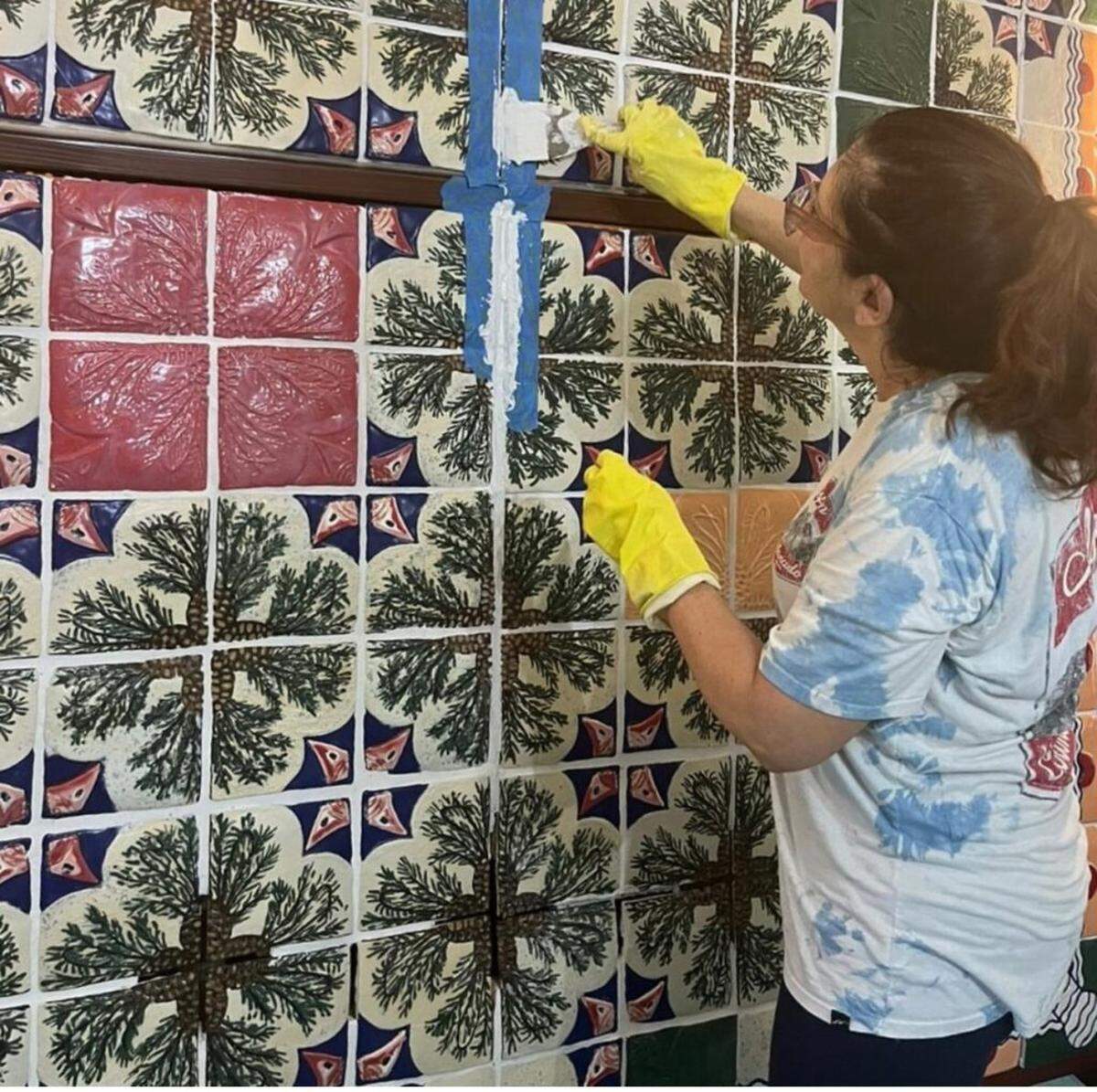 Artist Enma Saiz re-grouts seam lines in situ. The tiles were installed in components for easy transport. Saiz had to chisel the components and grout them apart in order to separate them for transportation and installation. She then re-grouted the cracks in the seams on site.