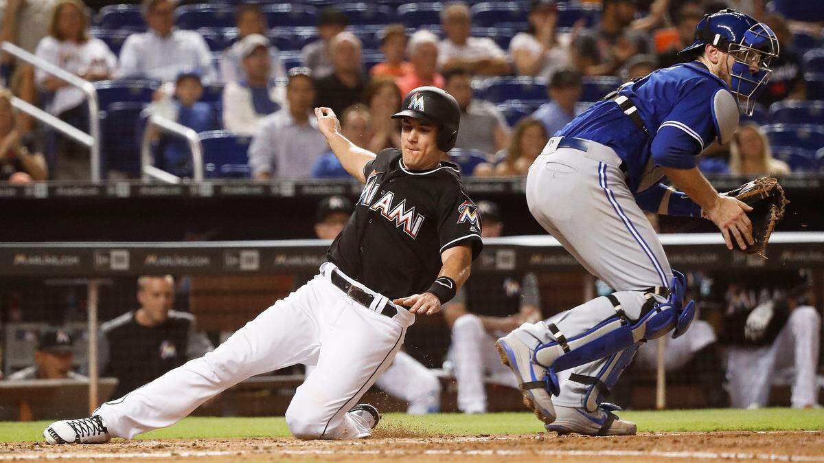 Miami Marlins’ J.T. Realmuto, left, slides into home to score during the fifth inning of a baseball game against Toronto Blue Jays catcher Danny Jansen, Friday, Aug. 31, 2018, in Miami.