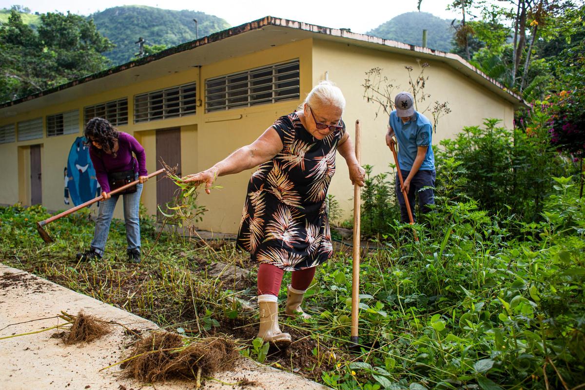 Community leader, Carmen Ana Acevedo [center], cleans out an area of the ‘Escuelita de la Tierra’ project at Barrio Cacao in Orocovis, Puerto Rico, on September 18, 2021. Also pictured, [L] Noelia Martinez and Ryan Acevedo.