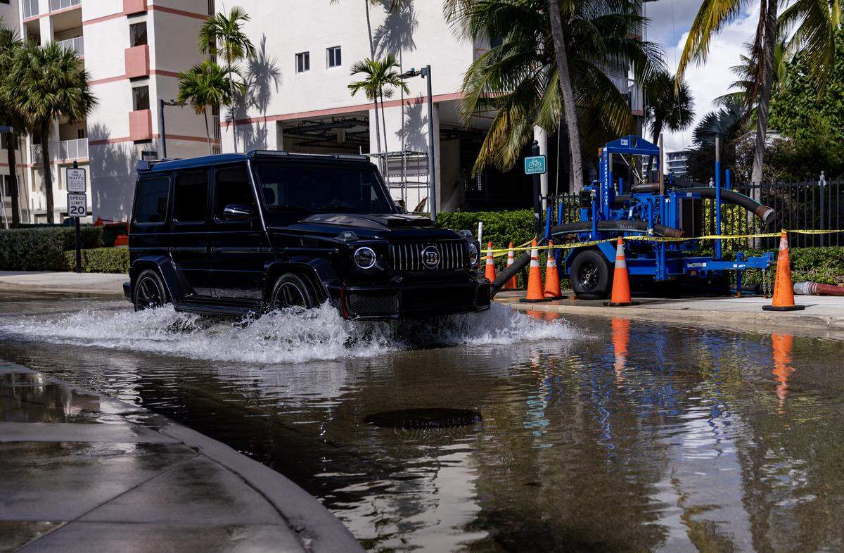 Una bomba de agua funciona mientras un automóvil avanza a través de las aguas de la inundación causada por la marea alta en la intersección de North Bay Road y 183rd Drive en Sunny Isles Beach, Florida, el lunes 6 de octubre de 2025.