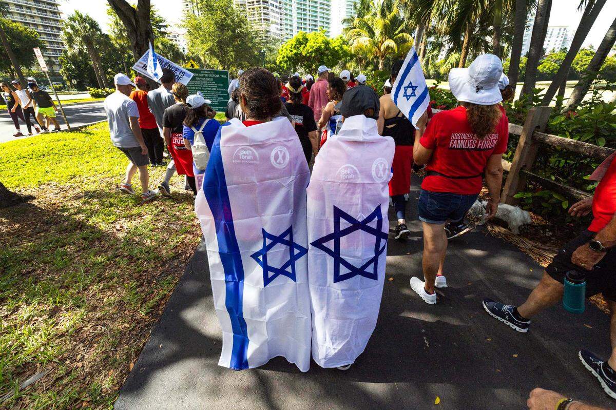Manifestantes portan banderas israelíes mientras caminan por la acera durante la caminata solidaria Run for their Lives para concientizar sobre los 58 rehenes que aún permanecen retenidos en Gaza, en Aventura Circle, el domingo 8 de junio de 2025, en Aventura, Florida.