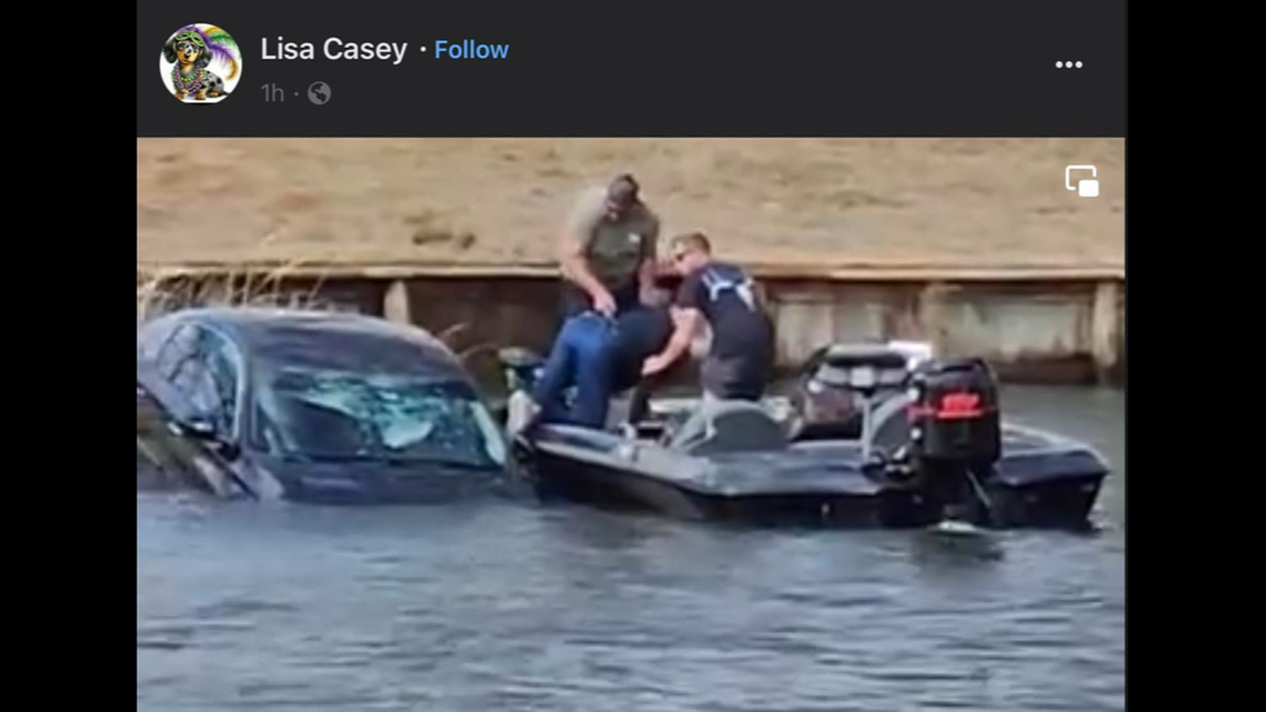 This image shows the two fisherman pulling the 80-year-old driver out of the car as it continued to settle into the river.