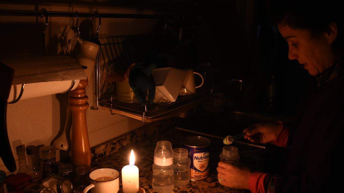 A woman prepares milk bottles using candles at her home in Montevideo during a power outage.