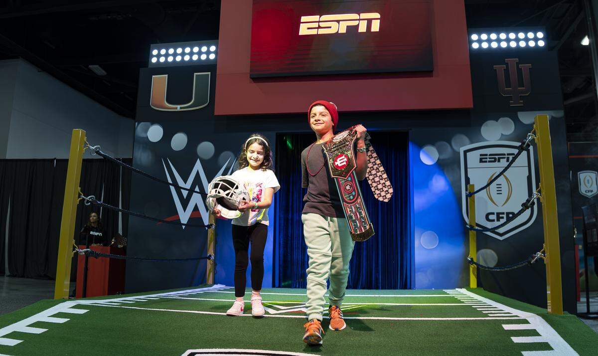 Nicholas Ramirez, 8, and his sister, Alexa Ramirez, 6, hold props and strike poses for a video while visiting the Playoff Fan Central at the Miami Beach Convention Center on Friday, Jan. 16, 2025, in Miami Beach, Fla. Fans can visit the event ahead of the College Football Playoff National Championship Game between the Miami Hurricanes and the Indiana Hoosiers and enjoy a variety of family-friendly interactive experiences.