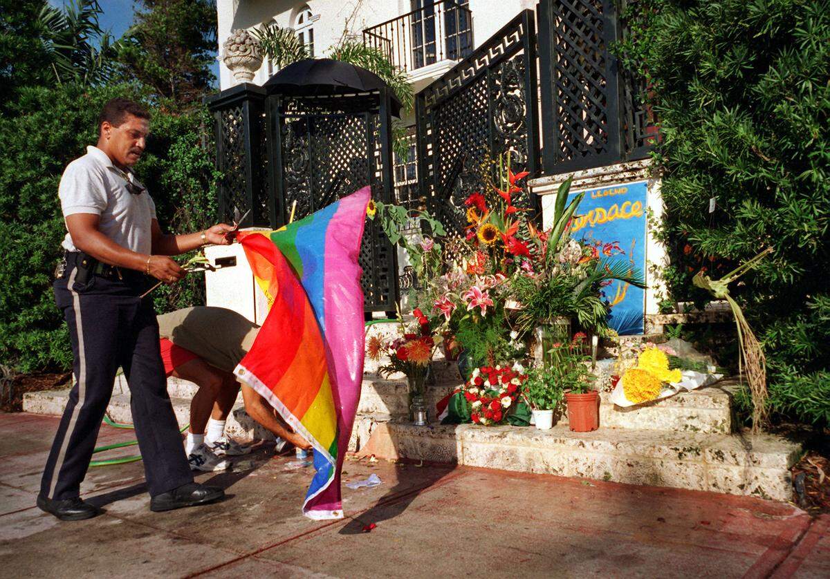 In this file photo from July 22, 1997, a private armed security guard removes a flag left by an admirer in front of the public makeshift memorial for Gianni Versace, the internationally known fashion designer who was killed on his mansion’s steps a week earlier by Andrew Cunanan.
