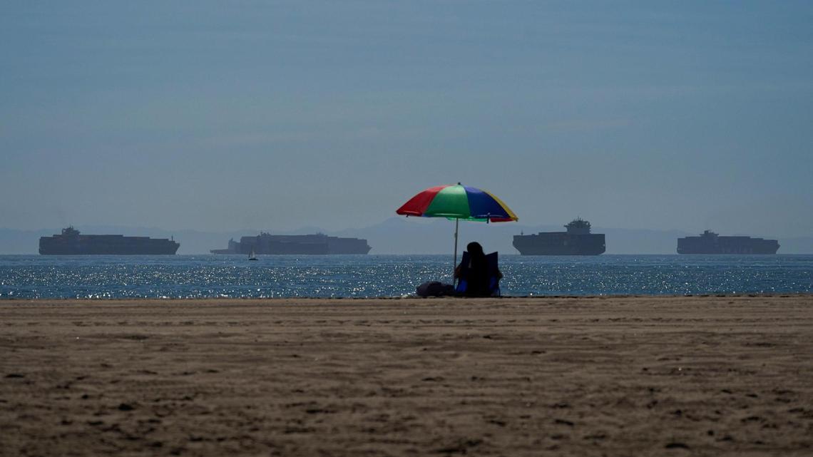 A person sits on the beach in Seal Beach, California, on Friday, Oct. 1, 2021, as container ships waiting to dock at the ports of Los Angeles and Long Beach are seen in the distance. With three months until Christmas, toy companies are racing to get their toys onto store shelves as they face a severe supply network crunch. Toy makers are feverishly trying to find containers to ship their goods while searching for new alternative routes and ports.
