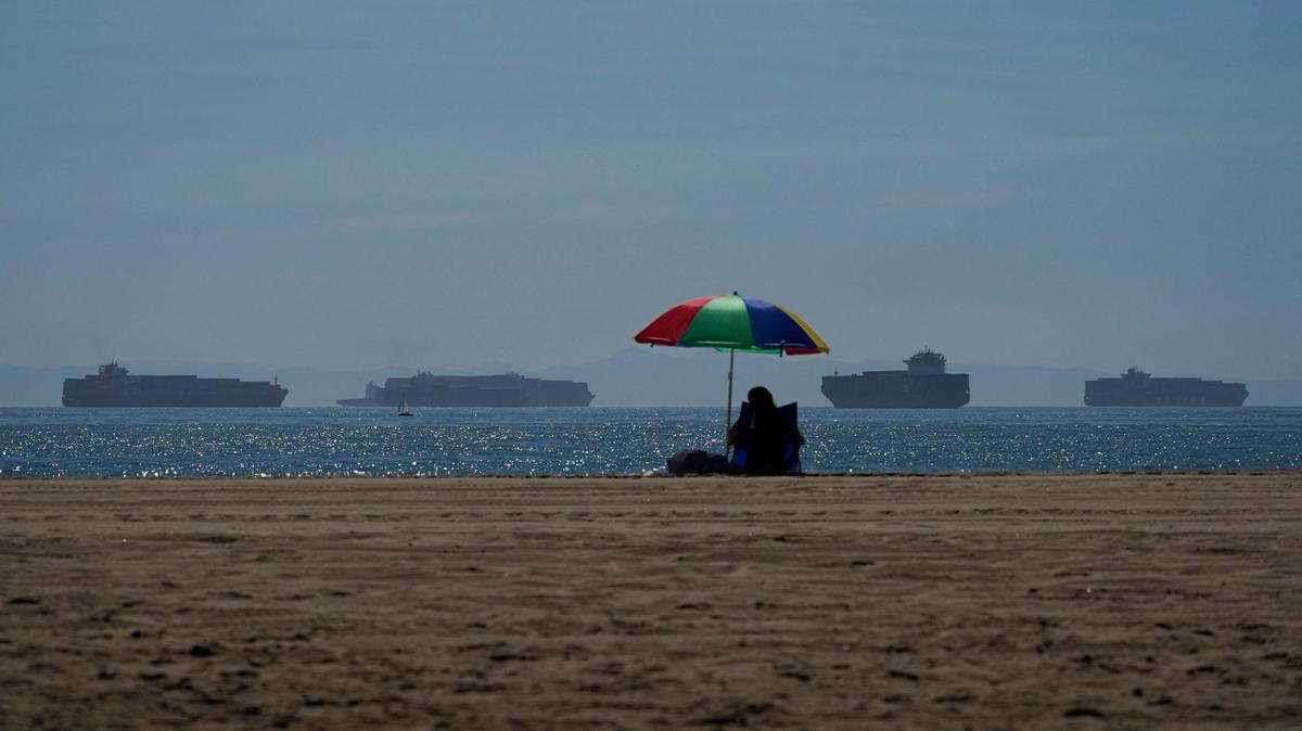 A person sits on the beach in Seal Beach, California, on Friday, Oct. 1, 2021, as container ships waiting to dock at the ports of Los Angeles and Long Beach are seen in the distance. With three months until Christmas, toy companies are racing to get their toys onto store shelves as they face a severe supply network crunch. Toy makers are feverishly trying to find containers to ship their goods while searching for new alternative routes and ports.
