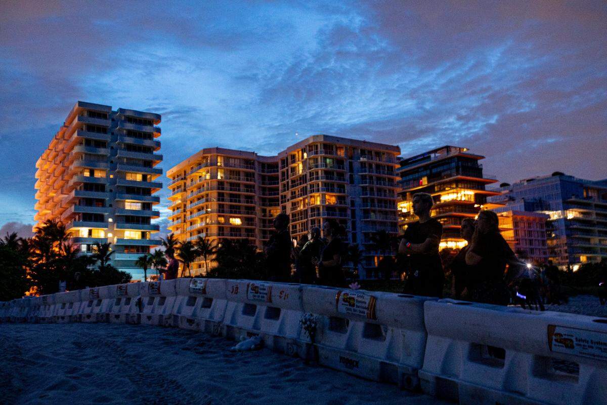 People watch from behind a police barricade on the beach as Florida Urban Search and Rescue teams work to remove debris from the partially collapsed Champlain Towers South condo as the sun sets in Surfside, near Miami Beach, Florida, on Monday, June 28, 2021.
