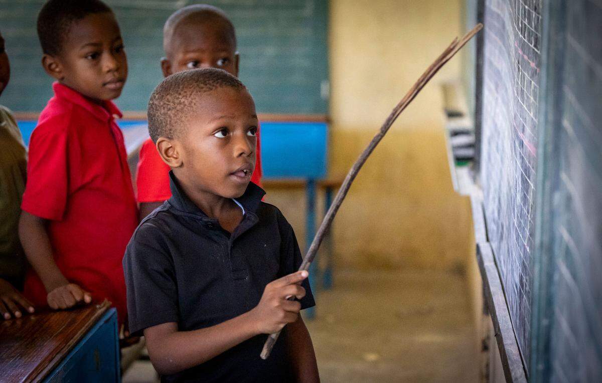 A first grader boy uses a small tree branch as a pointer as he recites in front of class during summer classes at Ecole National Louis Borno de Léogâne in Léogâne, Haiti.