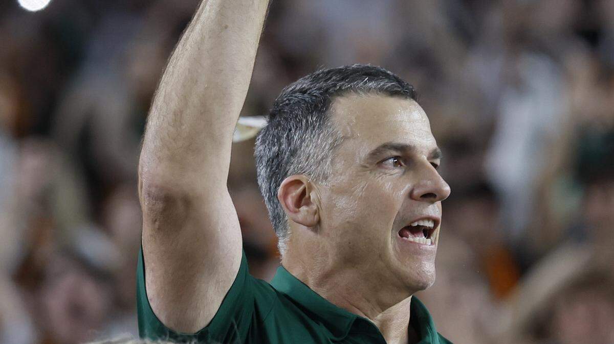 Miami Hurricanes head coach Mario Cristobal raises the diamond-encrusted football that is fully removable from the Fiesta Bowl Trophy, as the team celebrates on stage after defeating the Mississippi Rebels in the College Football Playoff semifinal at the Fiesta Bowl at State Farm Stadium on Friday, January 9, 2026 in Glendale, Arizona.