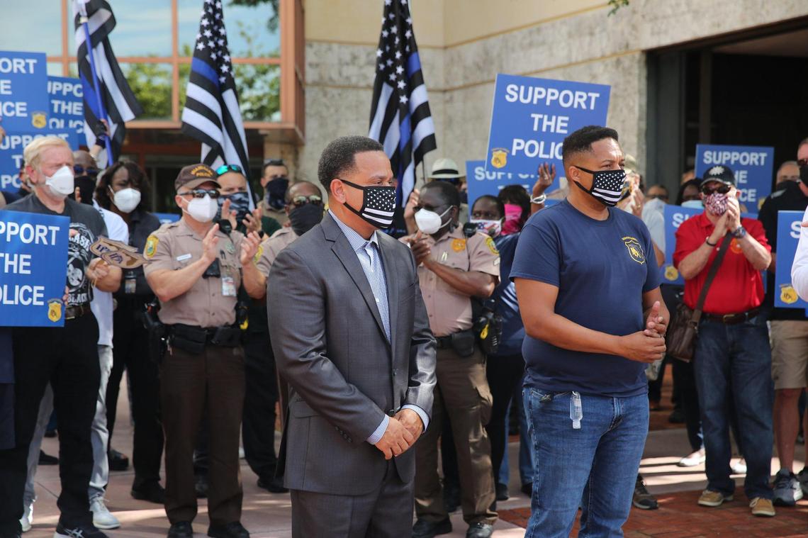 Miami-Dade Police Officer Antonio Rodriguez, left, is joined by South Florida Police Benevolent Association Executive Vice President John Jenkins, right, in front of a crowd of fellow officers clapping for him and showing their support before a hearing at police headquarters in Doral Tuesday morning August 18, 2020. The supporters were there to protest a hearing that could lead to the firing of Officer Rodriguez, who was seen slapping a woman on cellphone video footage.