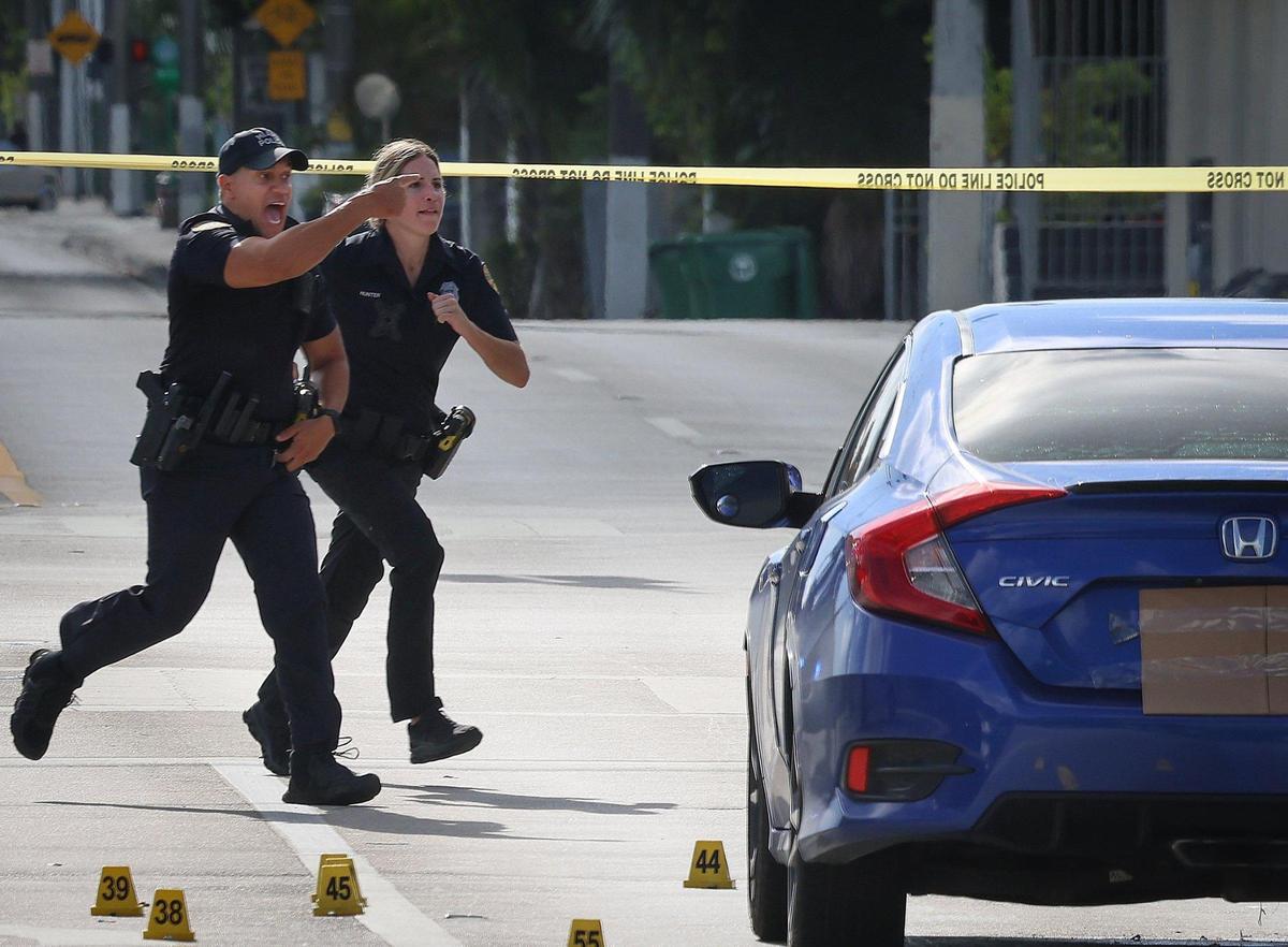 Two Miami police officers rush to intercept a pedestrian who ignored the crime tape where crime scene investigators were working near the intersection of Northwest 62nd Street and Northwest Second Avenue in Miami on Monday, June 16, 2025.