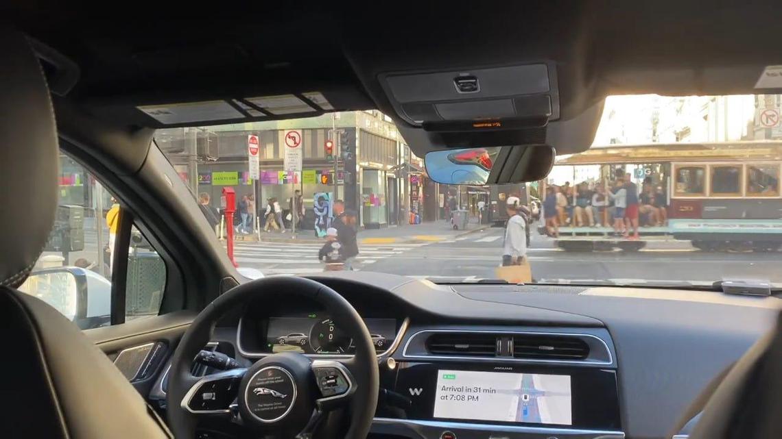A cable car crosses the path of a self-driving Waymo taxi in San Francisco.