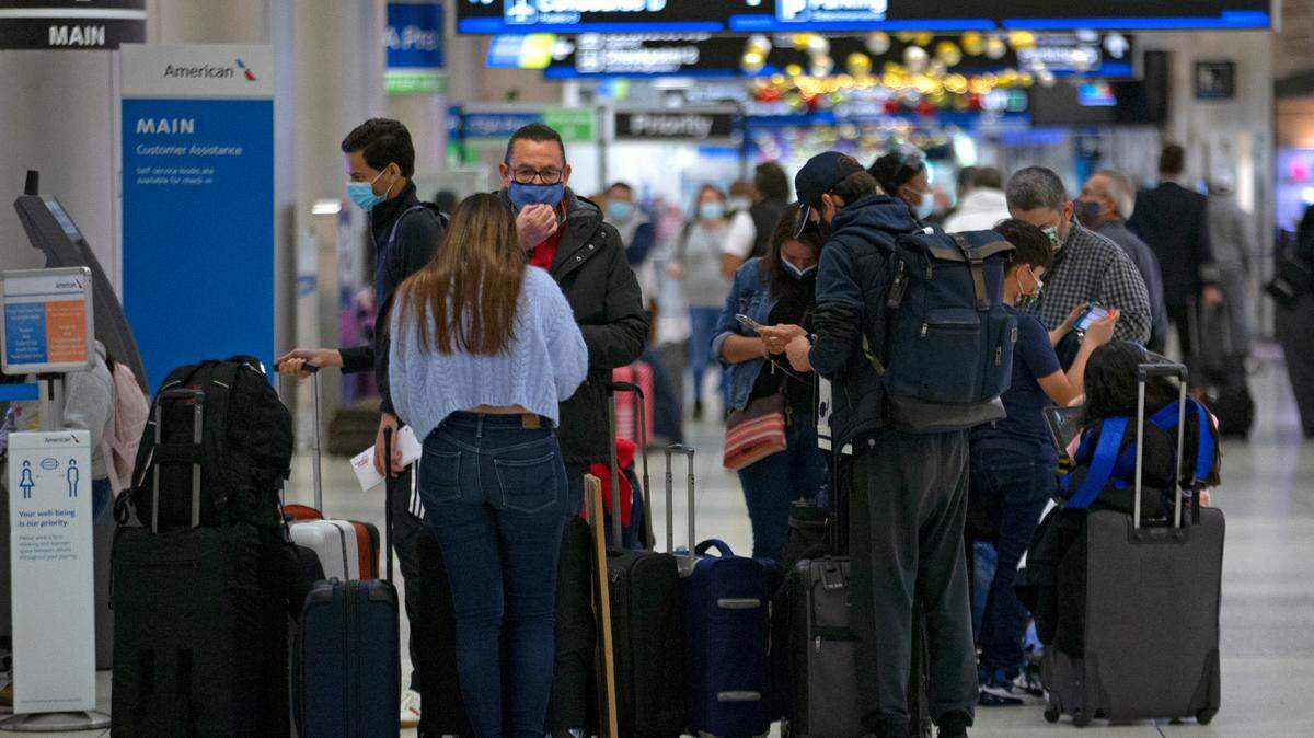 Travelers wearing protective face masks walk through Concourse D at Miami International Airport on Monday, Dec. 28, 2020.