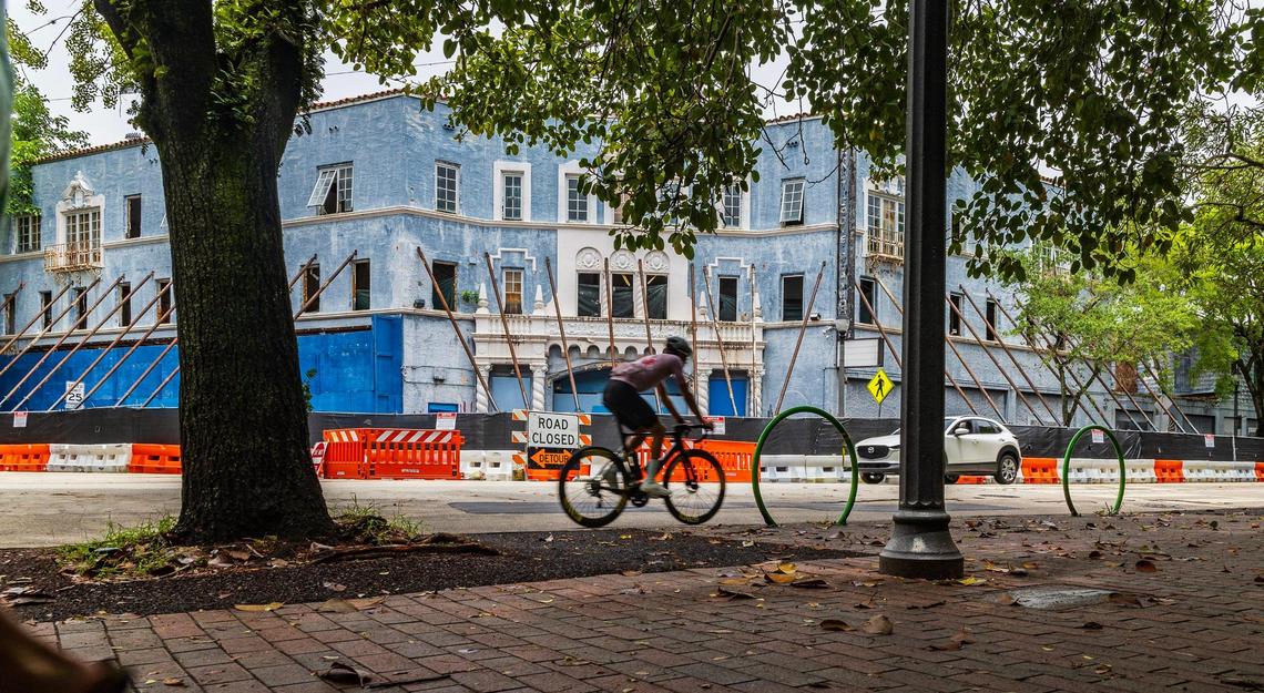 A cyclist rides on Main Highway past the historic Coconut Grove Playhouse in 2024. The theater’s facade has been reinforced with temporary beams since a contractor’s error during interior demolition work caused a partial ceiling collapse.