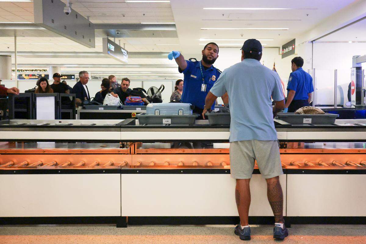 A TSA agent signals as a traveler places his personal belongings inside a bin on a lane with an automated bin return system during a standard security screening at checkpoint 2 at Miami International Airport on Tuesday, Nov. 25, in Miami, Fla.