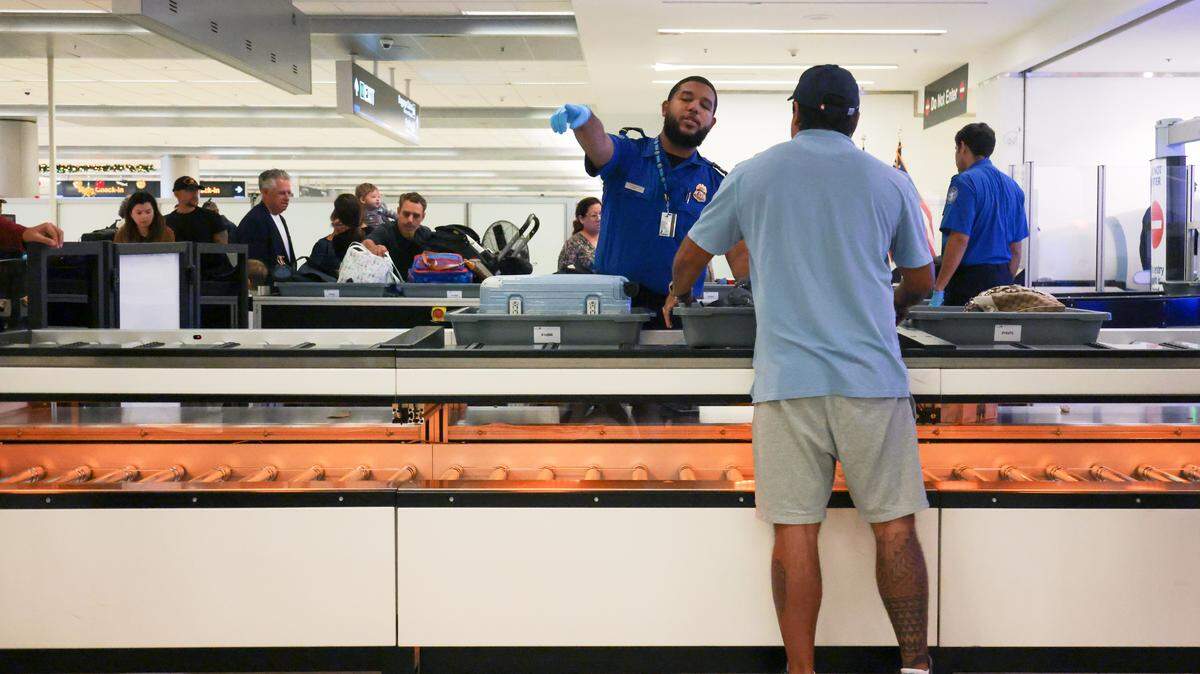 A TSA agent signals as a traveler places his personal belongings inside a bin on a lane with an automated bin return system during a standard security screening at checkpoint 2 at Miami International Airport on Tuesday, Nov. 25, in Miami, Fla.