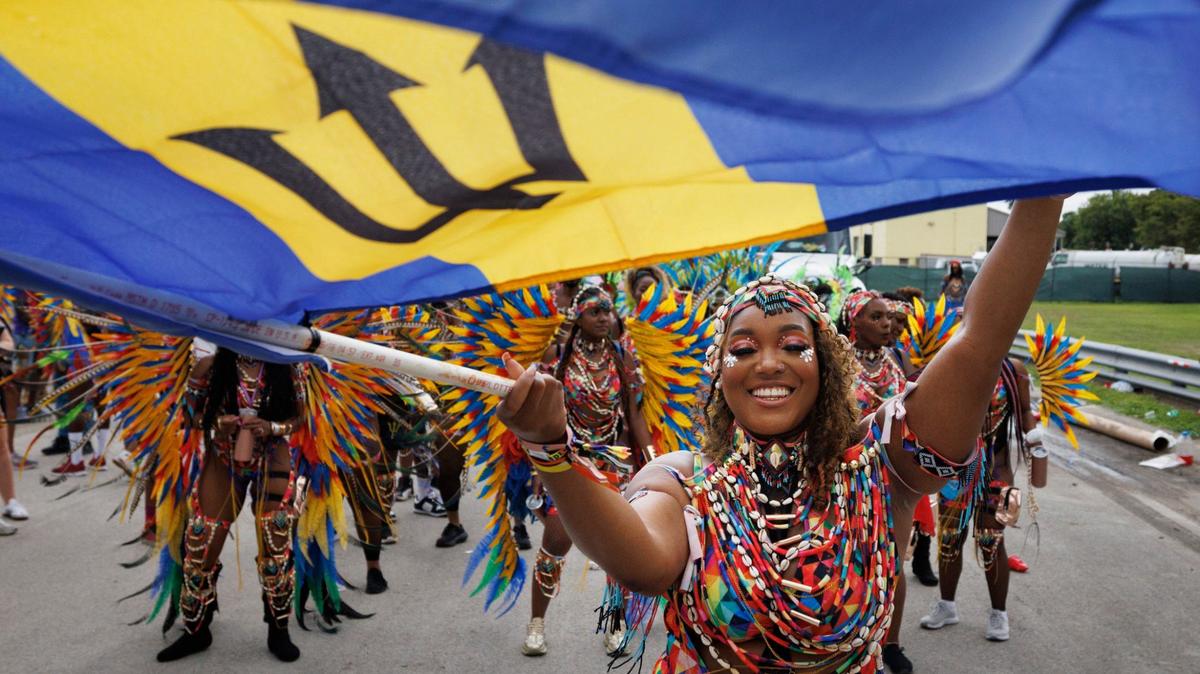 Chanel Osbourne, section leader also known as “queen”, leads the BFE MAS band in the Parade of Bands while waving a Barbados flag at Miami Carnival on Sunday, Oct. 13, 2024, at Miami-Dade County Fair Expo.
