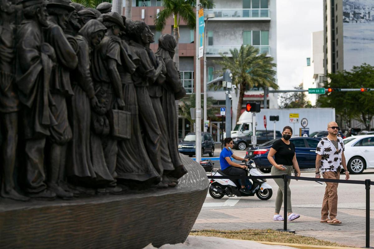 Pedestrians make their way past the traveling bronze sculpture titled “Angels Unawares,” at Bayfront Park in downtown Miami on Wednesday, February 10, 2021. The life-sized sculpture will be open to the public daily for viewing until April 8. The sculpture weighs four tons and is 20-feet long. It features indigenous people, Jews fleeing Nazi Germany, Joseph, Mary, Jesus, and much more.