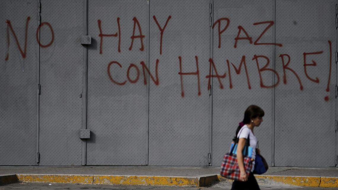 A pedestrian walks past a solid storefront security gate spray painted with a message that reads in Spanish: "There is no peace when there is hunger!"  in a file photo in Caracas, Venezuela, on July 26, 2017.