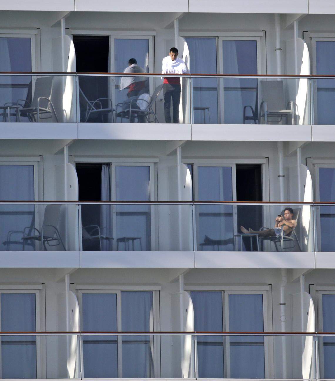Crew members stand outside on their balconies on the Norwegian Encore at PortMiami on Thursday, March 26, 2020.